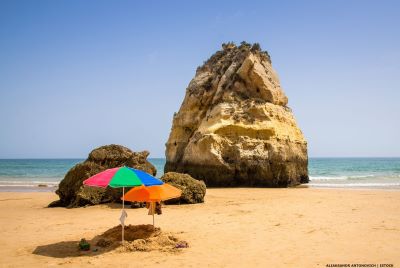 Two sun umbrellas on an empty beach with rock formation